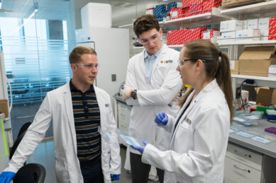 Three scientists in white coats chat in a lab 