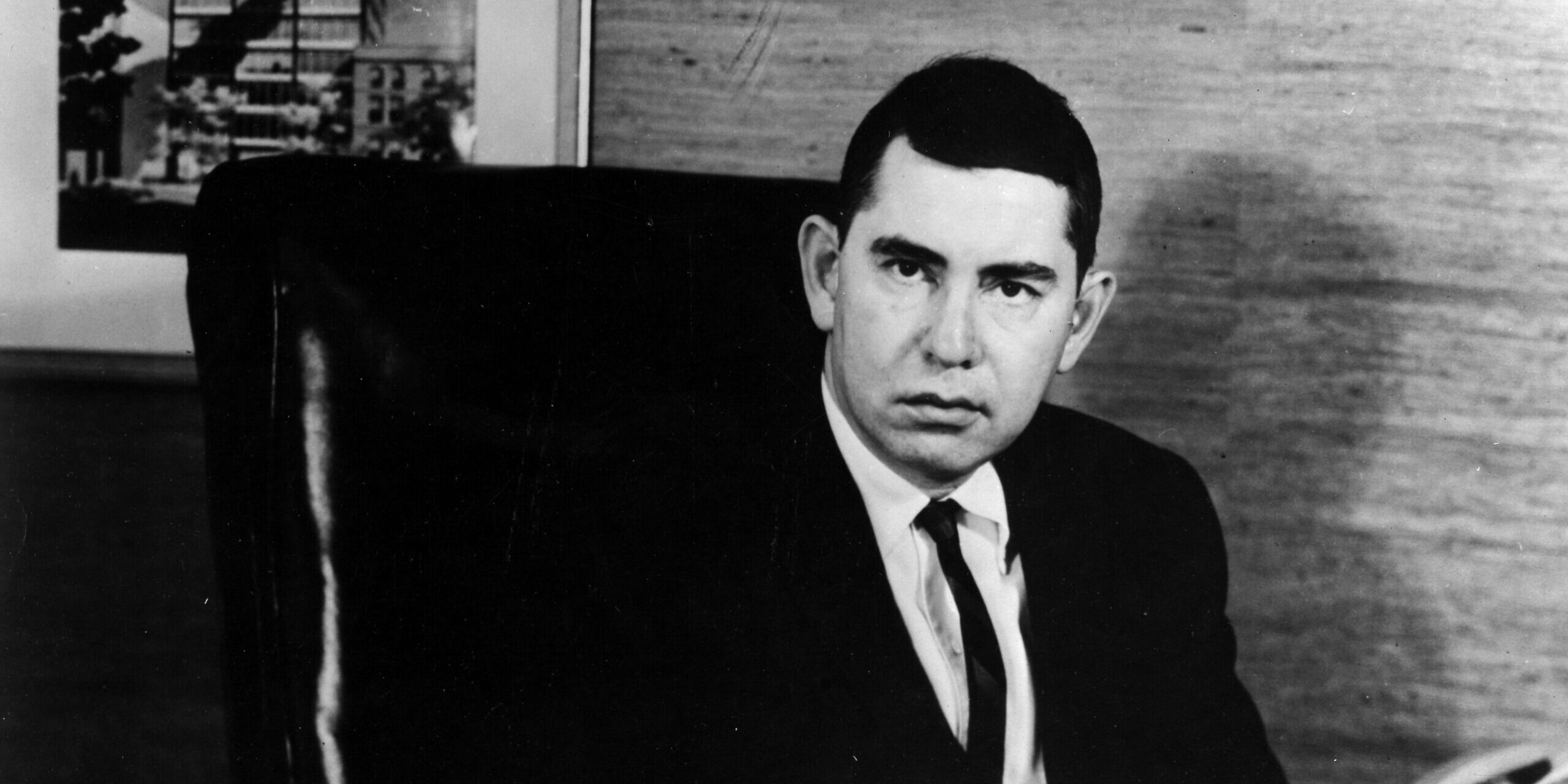 Black and white photo of Paul Cohen in a suit jacket and tie sitting in a desk chair