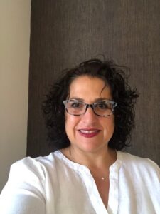 Headshot of occupational therapist Theresa Berner, a woman with shoulder-length dark brown curly hair, light skin, and tortoise shell glasses.