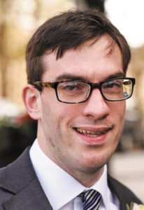 Headshot of Joel Cartner, a man with short brown hair, light skin, and tortoise-shell glasses.