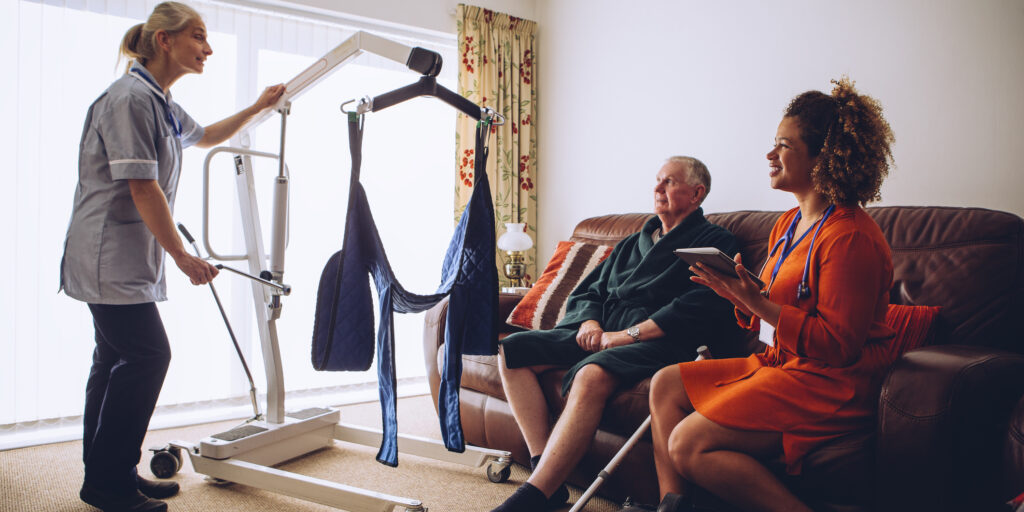 Two homecare nurses at an elderly mans house. They have a hoist set up.