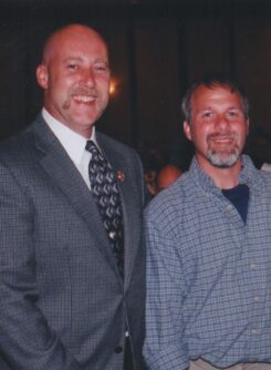 Two men stand next to each other smiling