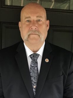 Headshot of a man in a suit coat and tie wearing a fire fighter pin