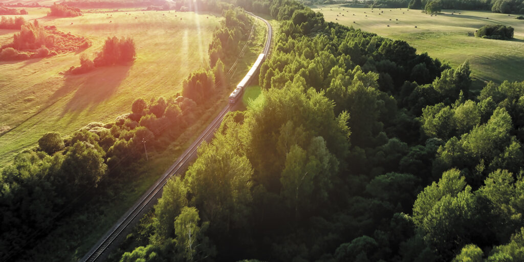 Aerial view of a train traveling through a lush, green landscape of forests and pastures.