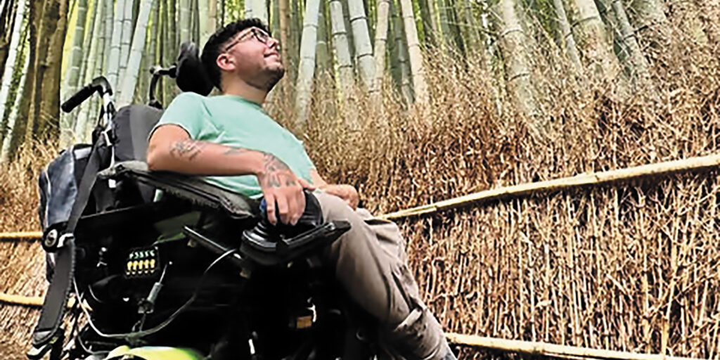 Cory Lee, a young man living with spinal muscular atrophy, looks up at the scenery as he drives his power wheelchair on a path through a bamboo forest.