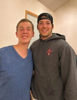 A teenager in a blue T-shirt smiles next to a young man in an IAFF sweatshirt and black hat