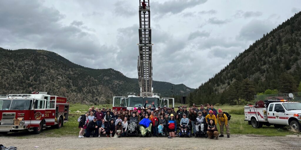 A large crowd of MDA Summer Camp campers and volunteers pose in front of a fire truck with its ladder raised