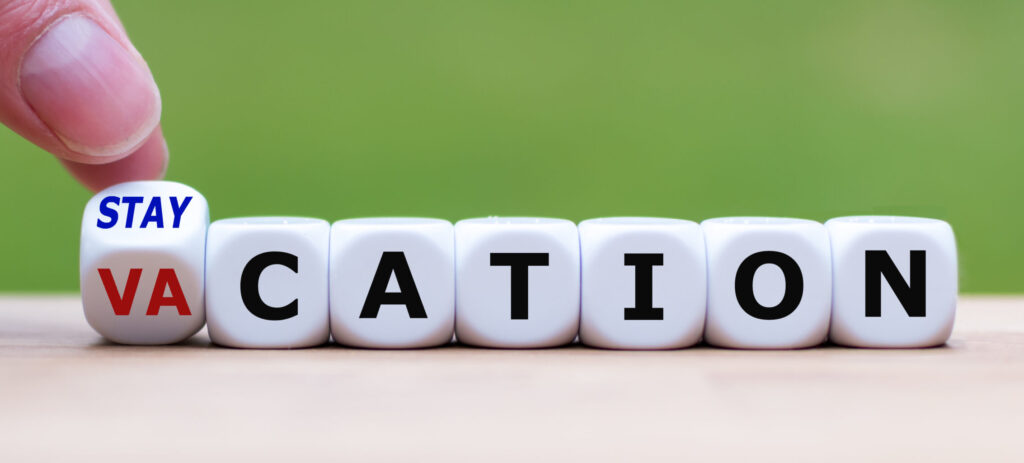 Hand turns a dice and changes the expression "vacation" to "staycation".