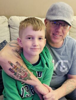 A man in a baseball hat smiles with his arm around a young boy sitting next to him