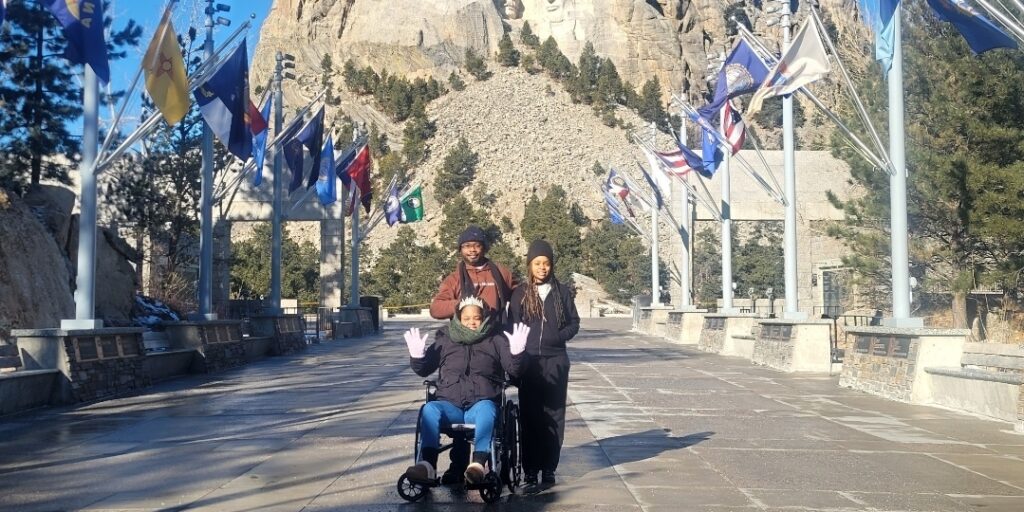 Tamara_South Dakota Tamara Blackwell, in a wheelchair, and her two travel companions pose with Mt. Rushmore in the background.