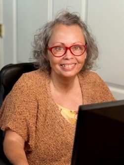 Photo of Lorraine Woodward wearing red glasses and an orange shirt