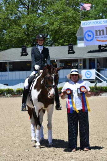A young woman on a horse poses next to an older woman holding ribbons
