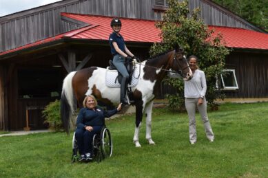 A young girl sits on a horse with a woman in a wheelchair and a woman standing next to her