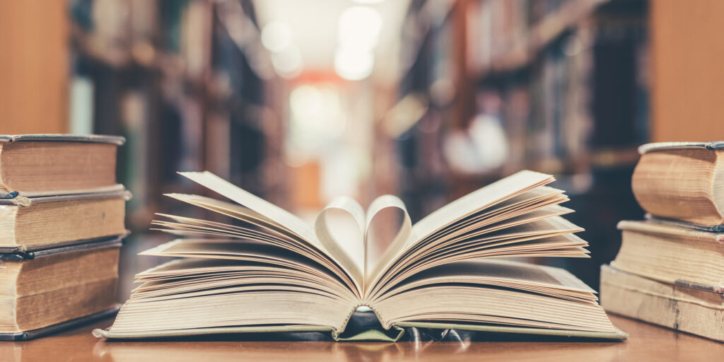 Book with open page of literature in heart shape and stack piles of textbooks on reading desk in library