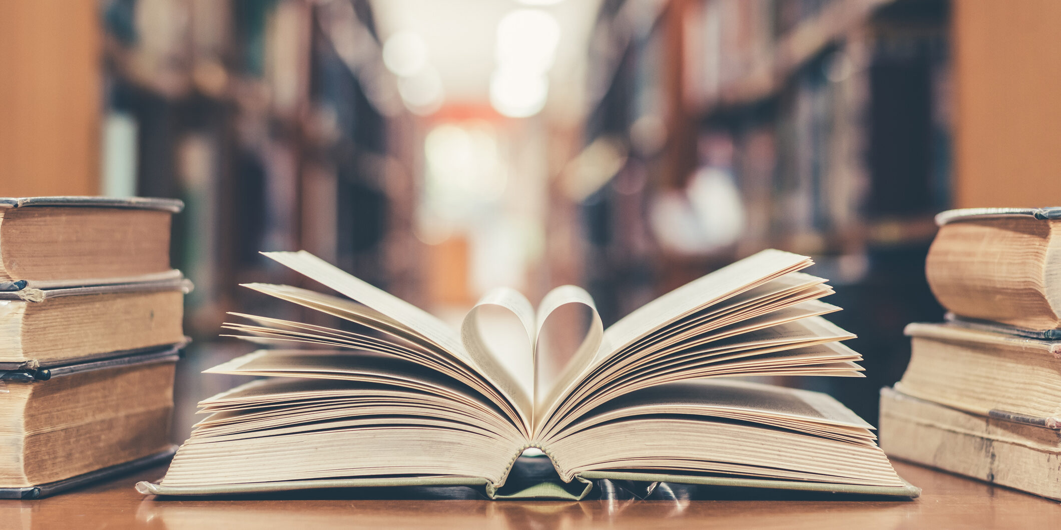 Book with open page of literature in heart shape and stack piles of textbooks on reading desk in library