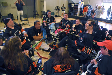 A team of power hocket players in black jerseys and power wheelchairs gather together. 