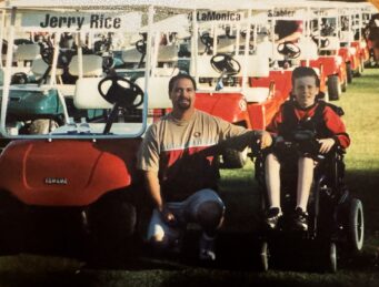 A young man in a wheelchair next to an older man in front of golf carts