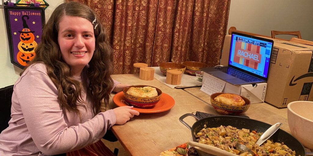 Gabby DiSalvo, seated in her wheelchair at a kitchen table, shows off a finished meal she cooked.