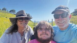 Carrie Miceli and Stanley Nelson, who are both scientists and parents, pose outdoors on a sunny day with their adult son Dylan, who lives with Duchenne muscular dystrophy.