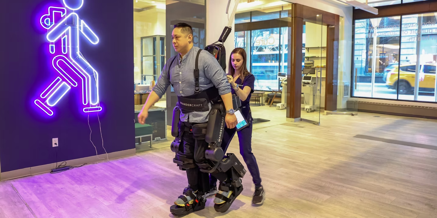 A patient walks using Wandercraft’s Atalante X hands-free exoskeleton under the supervision of a physical therapist at Walk in New York.