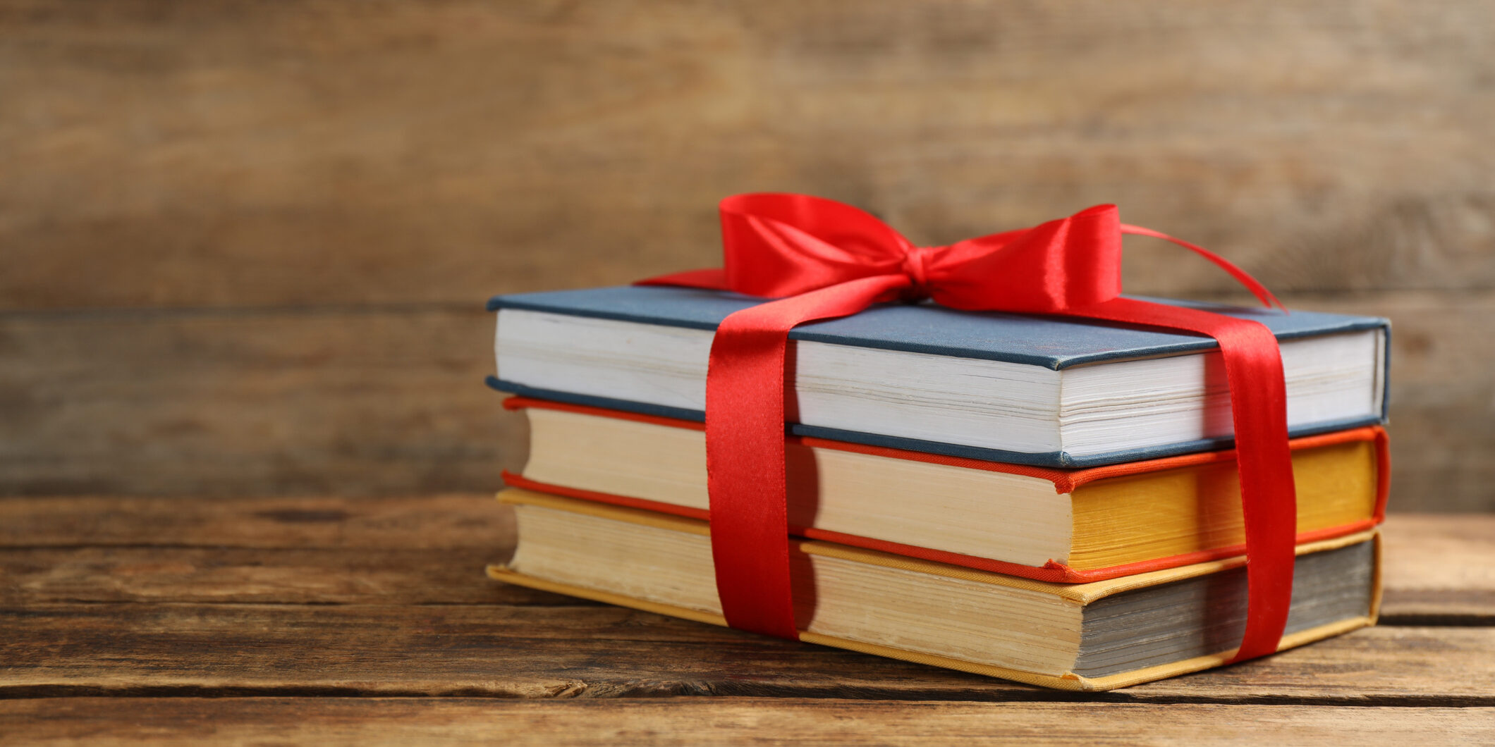 Different books tied with red ribbon on wooden table