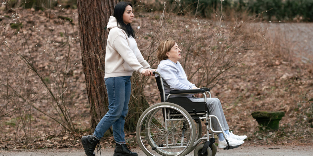 A heartwarming scene shows a caregiver pushing a wheelchair through a serene park filled with vibrant nature