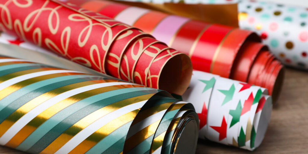 Different colorful wrapping paper rolls on wooden table, closeup