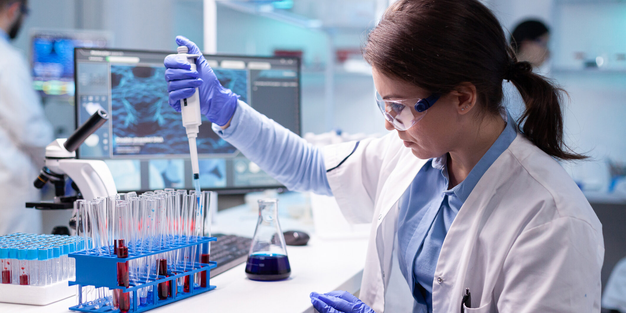 Concentrated professional woman scientist in laboratory working with a micropipette and a dropper.