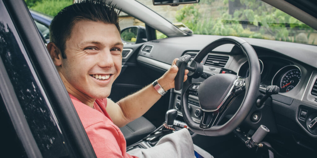 Quadriplegic man sitting in the seat of his customised control car. He is smiling for the camera.