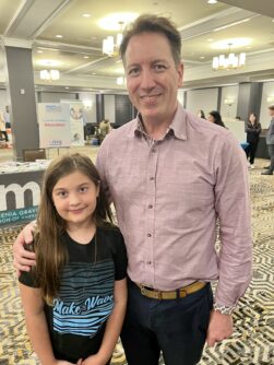 A young girl poses with a man in a button down shirt at a conference