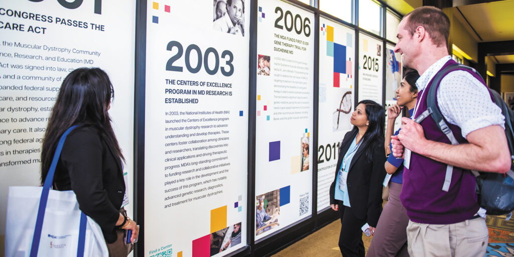 MDA Clinical & Scientific Conference attendees gather around a sign about MDA’s history supporting neuromuscular research.