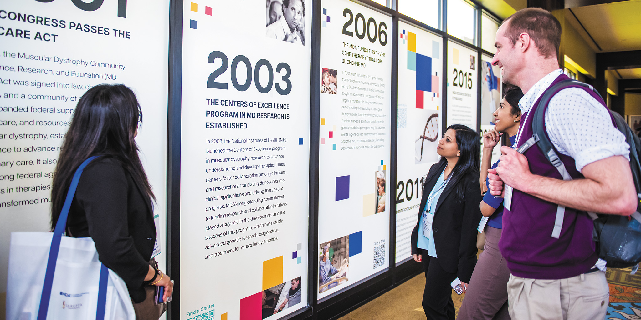MDA Clinical & Scientific Conference attendees gather around a sign about MDA’s history supporting neuromuscular research.