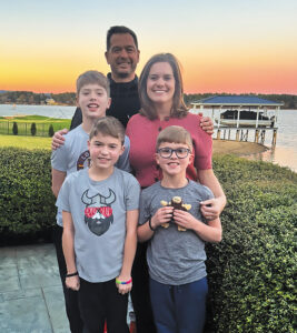 William Small, Alison Joseph, and their three sons stand in front of a lake at sunset.