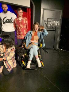Fiona Cauley sits in her wheelchair on stage with a small group of other comedians.