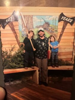 A dad stands next to his two children in front of a sign
