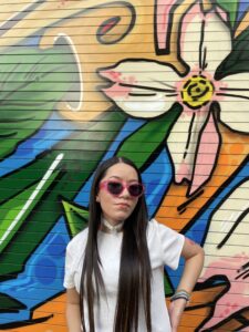 Stephanie posing in front of a colorful artistic street mural. 