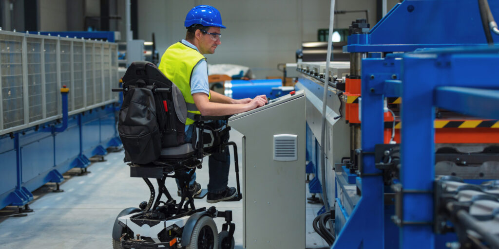 Man with disability in yellow vest, engineer in a factory unit checking a work process. inclusion and diversity concepts.