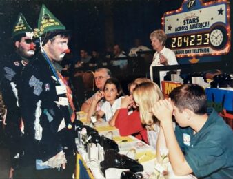 A photo of clowns standing in front of a table full of telephones and volunteers at the MDA Telethon