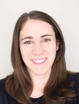 Headshot of a white woman with brown eyes and shoulder length brown hair wearing a black shirt 