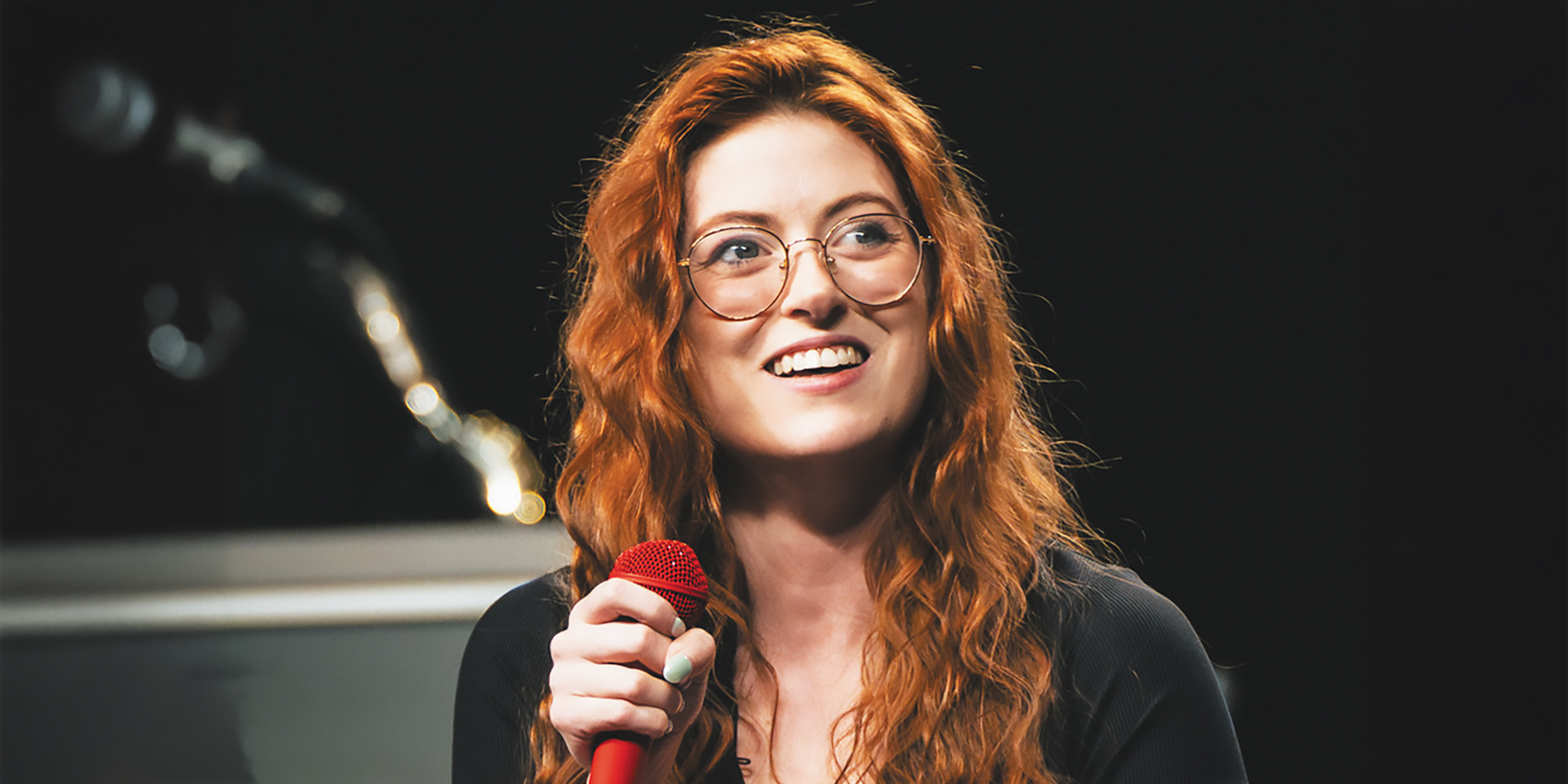 Closeup of comedian Fiona Cauley holding a red microphone while performing stand-up comedy.