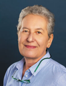 Headshot of Dr. Emma Ciafaloni wearing a blue shirt with glasses hanging around her neck against a dark background.
