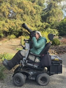 Paul Miller in a wheelchair viewing birds through a long lens mounted on his wheelchair.