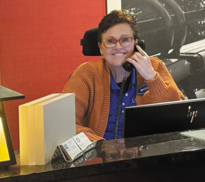Sharon Townsend sits behind a reception desk holding a phone to her ear and smiling at the camera.
