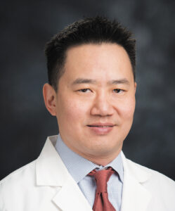 Headshot of dentist Michael Chan wearing a white lab coat against a dark background.