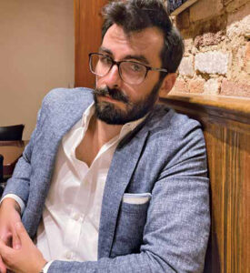 Closeup of Andrew Zaleski indoors wearing glasses and a blue jacket with a white pocket square.