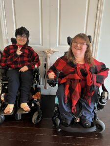 Katrina Gossett-Kelly and her son in powered wheelchairs smiling while wearing matching red and black plaid outfits.