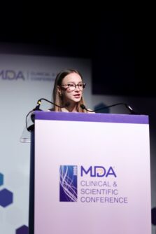 A young woman stands at a podium that reads MDA CLINICAL & SCIENTIFIC CONFERENCE