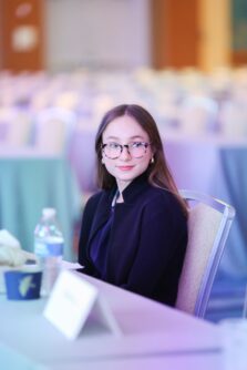 A young woman wearing glasses sits a table in a conference room