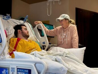 A mother stands by her adult son's bedside in the hospital