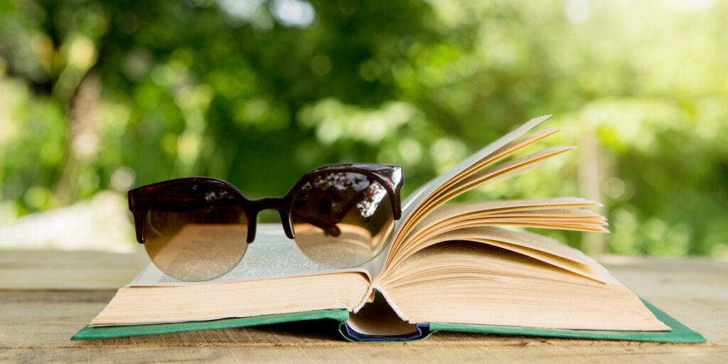 Open book and eyeglasses on a wooden table in a garden on a Sunny summer day